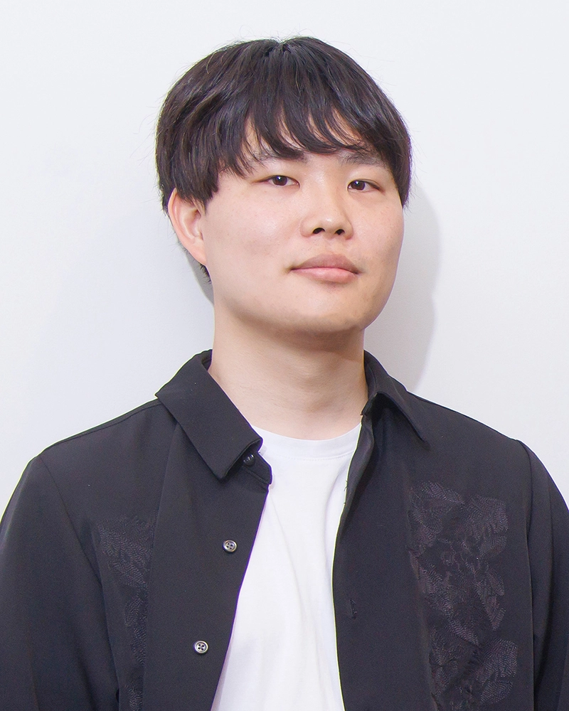 A person in a black shirt stands against a plain white background, looking directly at the camera