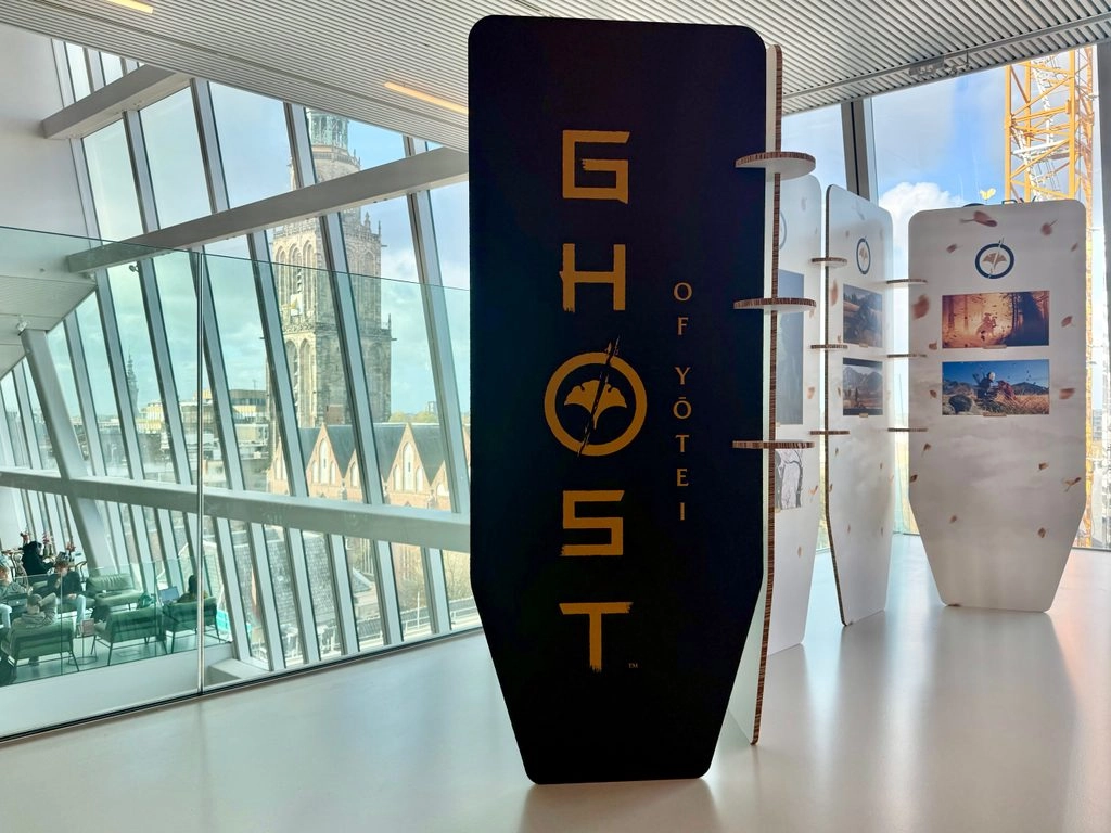 Display of Ghost of Yōtei promotional stand in a modern building with large windows and city view