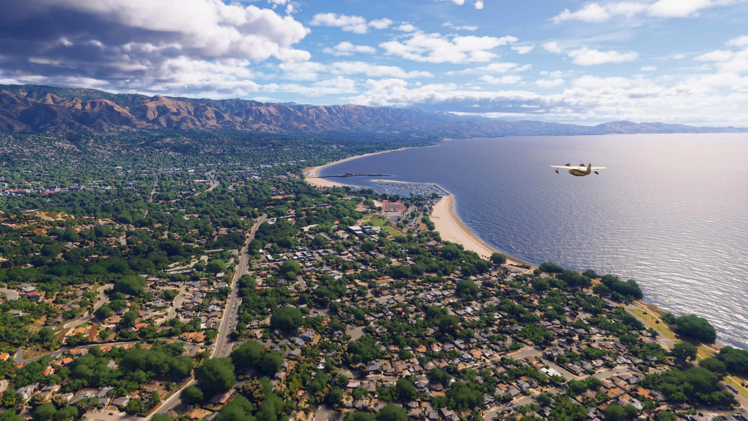 Scenic aerial view of a coastal California city with lush greenery, mountains, and a plane flying overhead