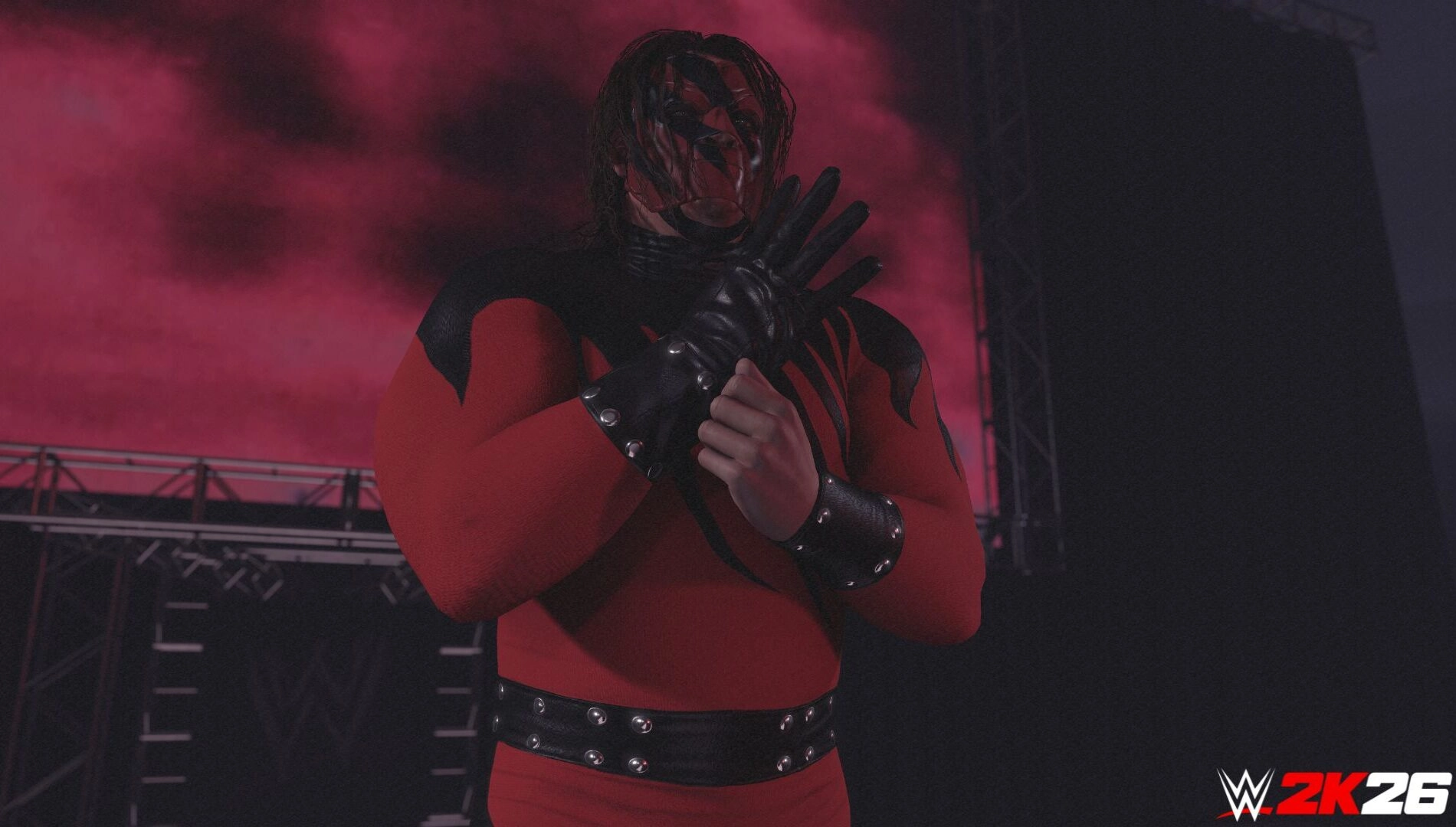 Wrestler in red and black attire stands on stage with a red-lit background, preparing for a match