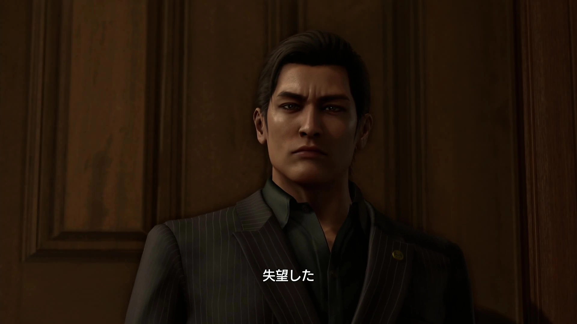 Yoshitaka Mine stands in a dimly lit room, wearing a suit, conveying a serious expression