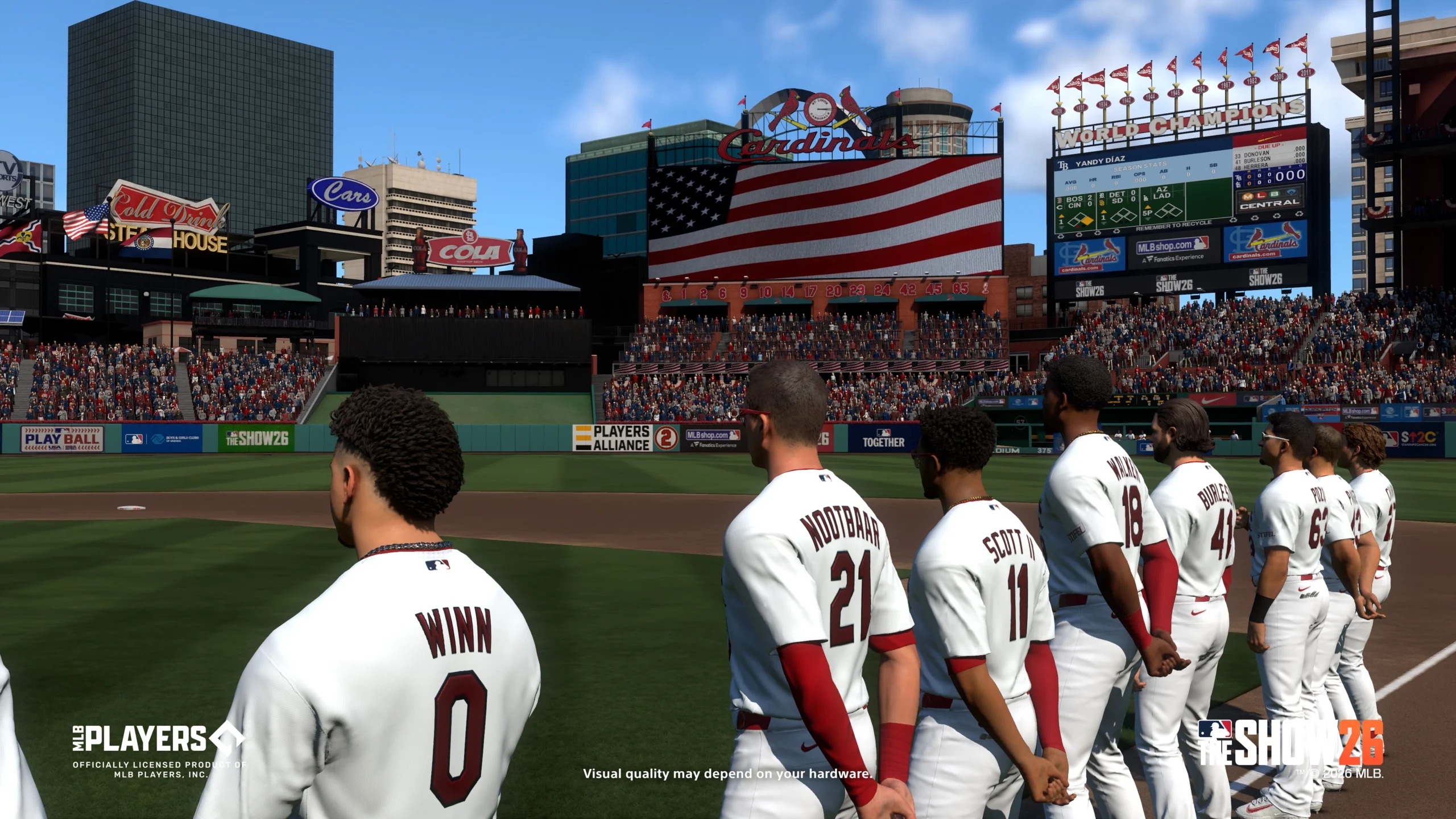 Baseball players stand on the field during the national anthem, with a large American flag displayed on screen