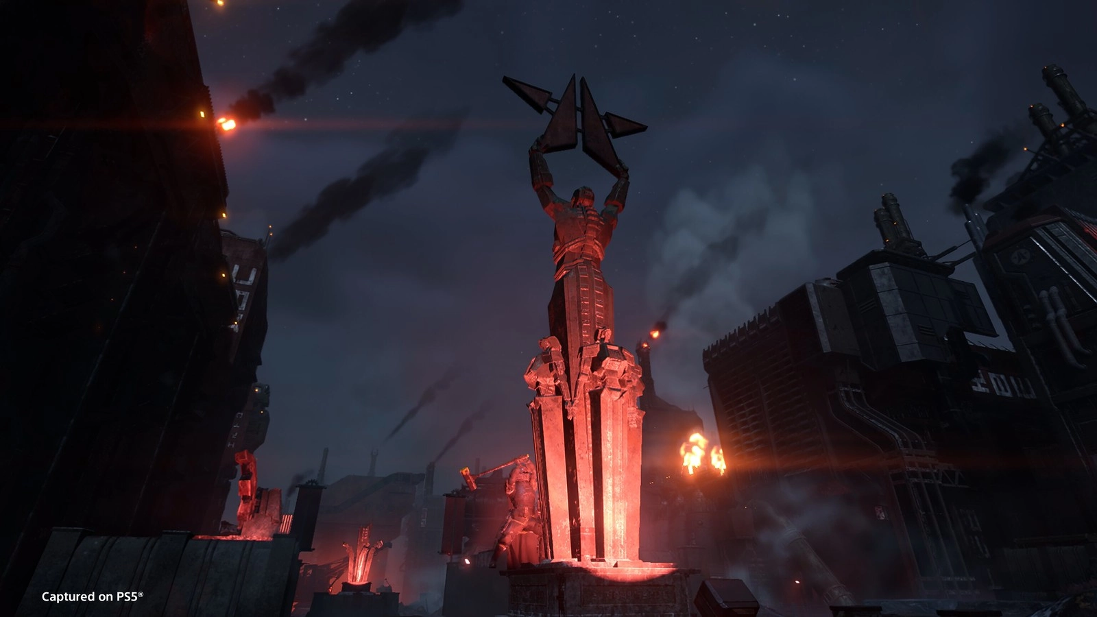 A towering statue in a dark, industrial cityscape, glowing red amidst smoke and factory structures