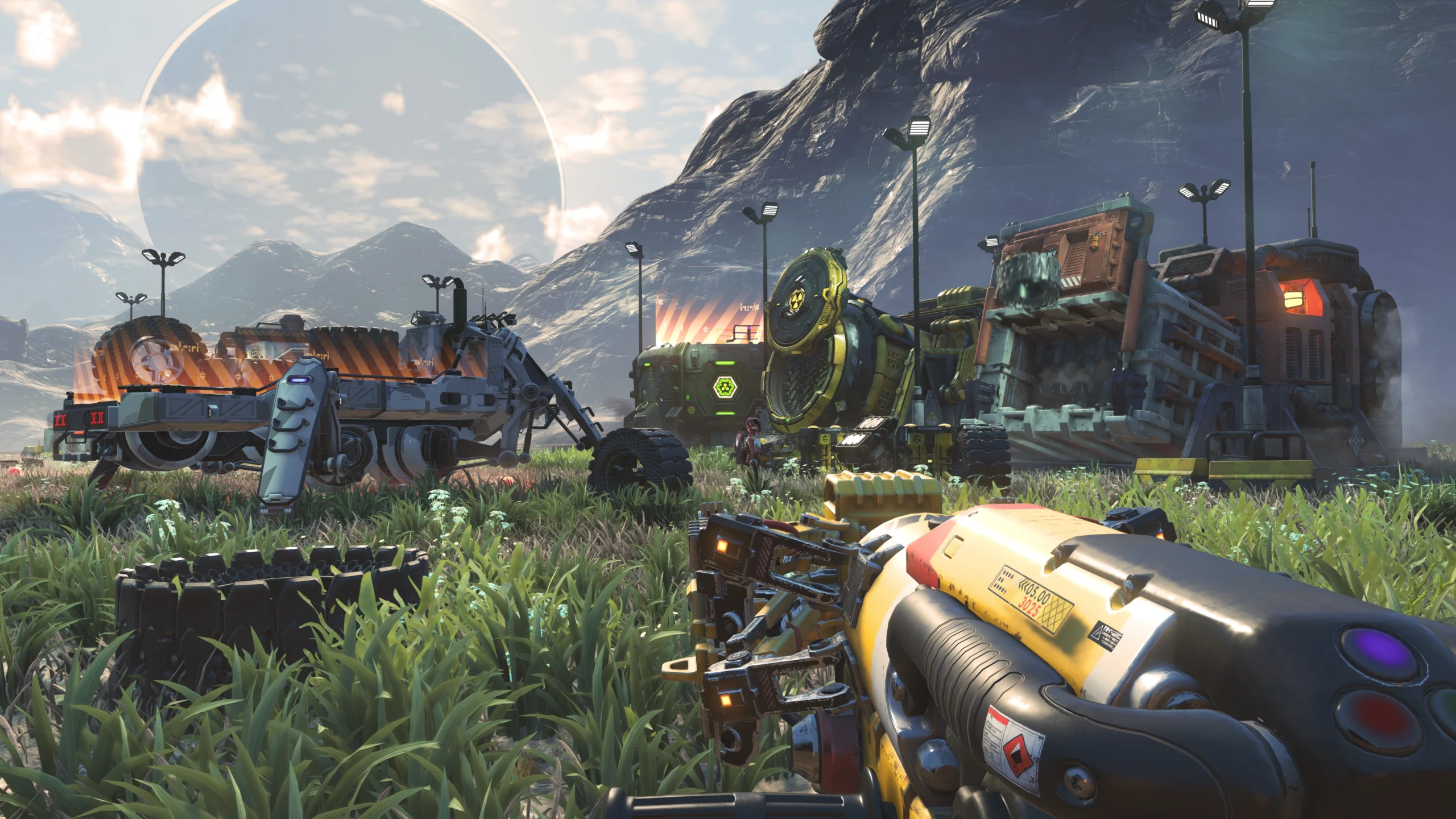 A player holds a gravity gun in No Man's Sky, facing futuristic trucks and machinery on an alien landscape