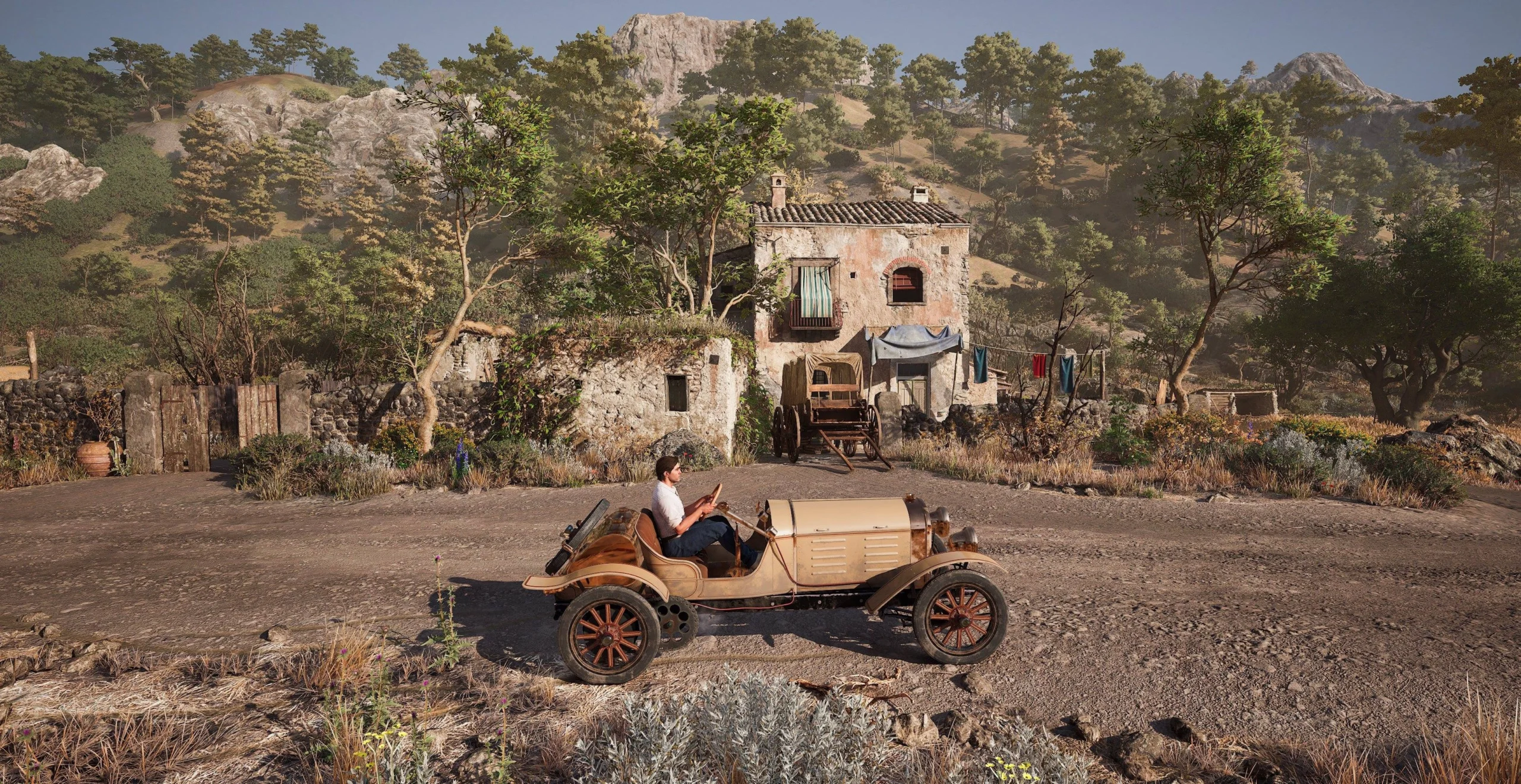 A vintage car parked on a rustic road in front of an old stone house surrounded by lush greenery