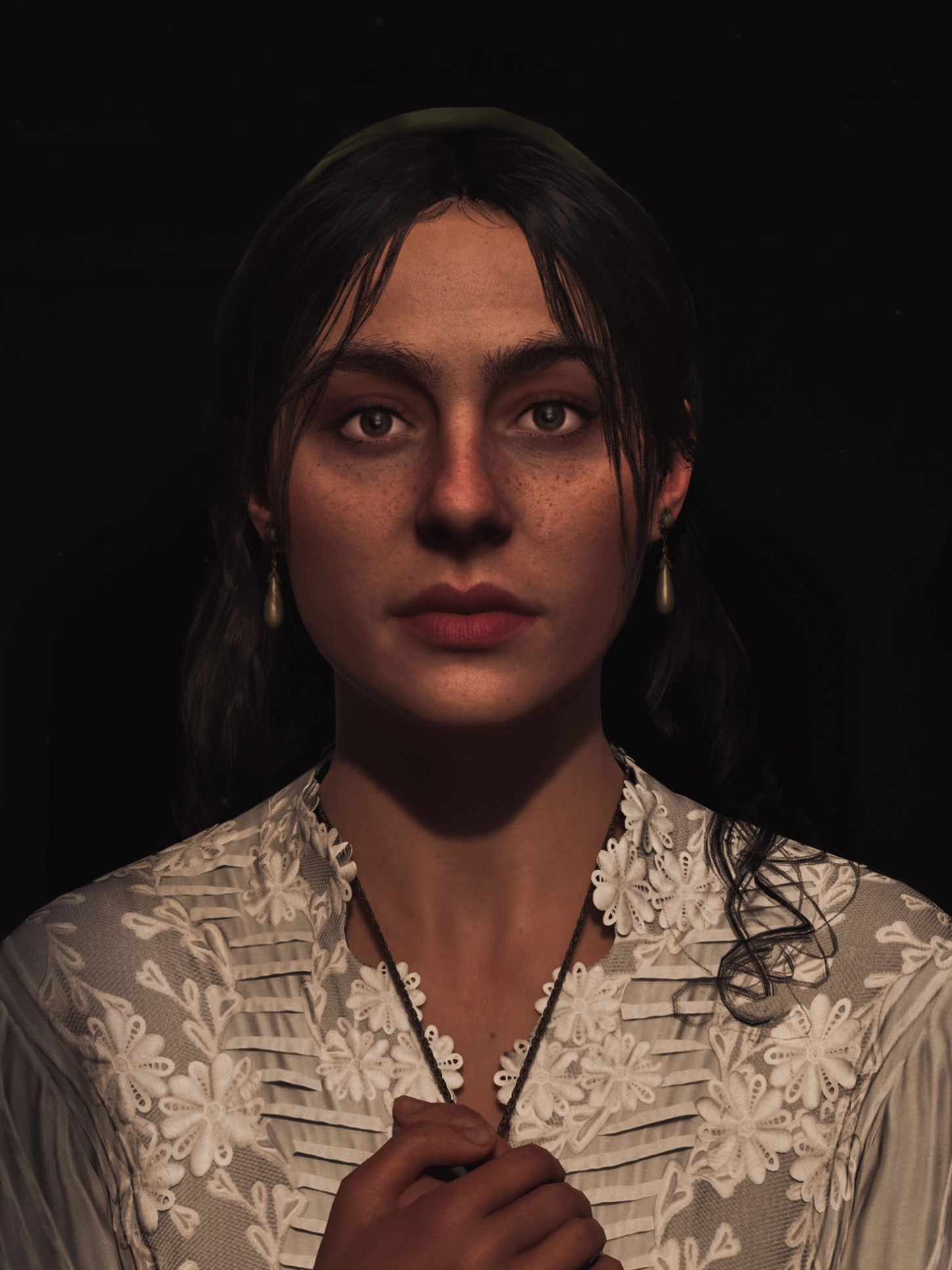 Woman with dark hair and floral blouse gazes forward, hands clasped, in dim lighting setting