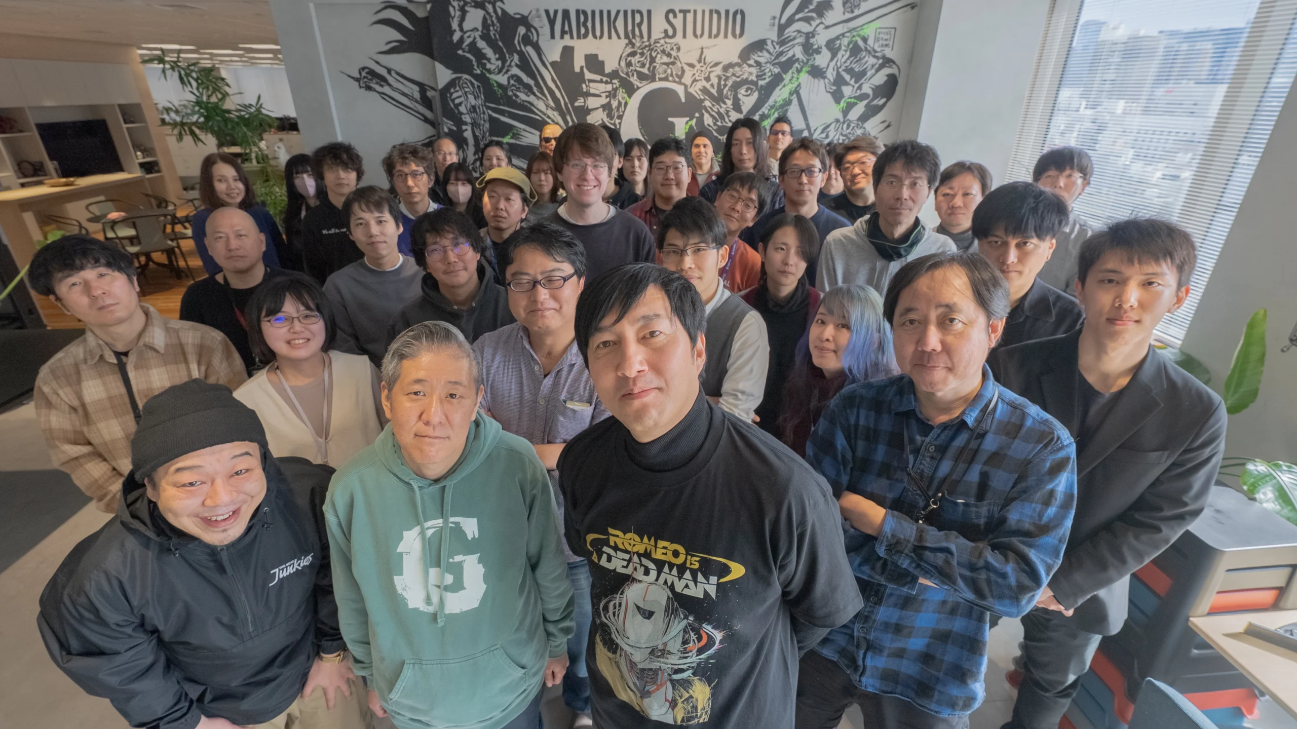 A group of developers at Yabukiri Studio, including Goichi Suda and Ren Yamazaki, posing together indoors