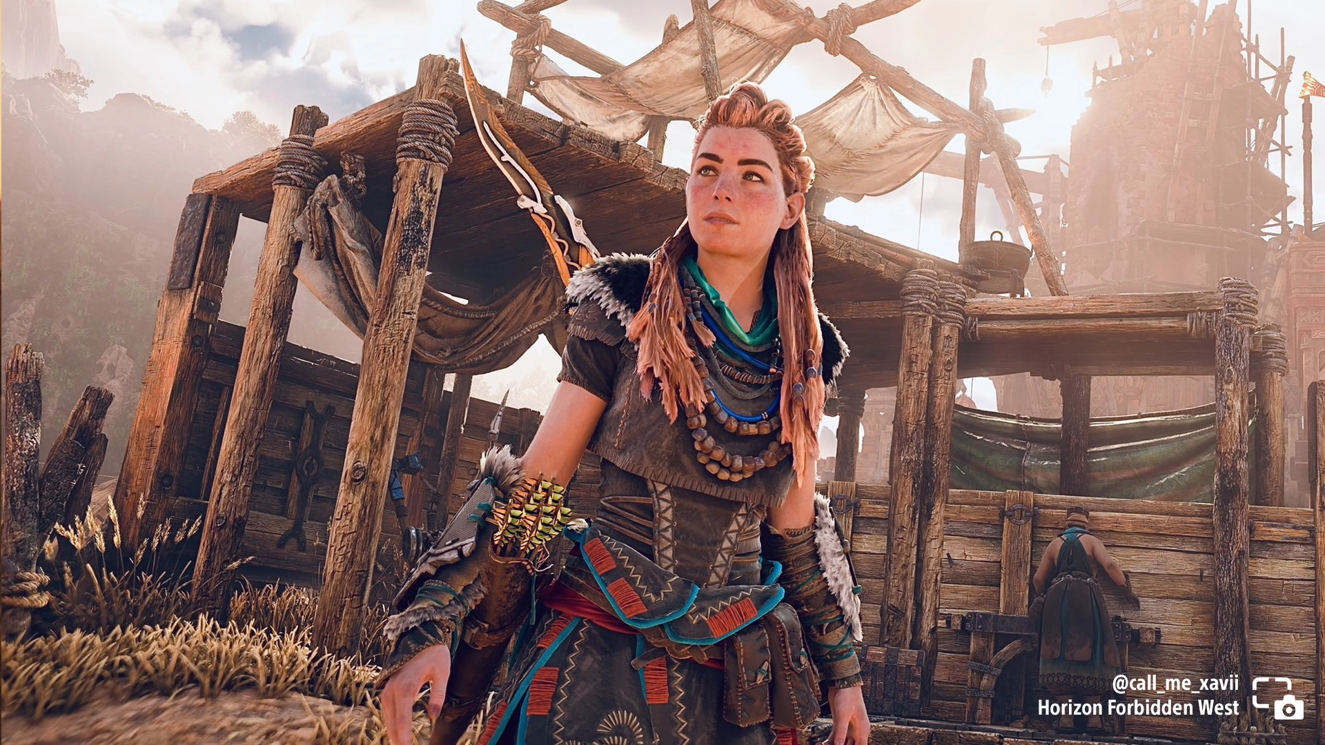 Aloy stands confidently outside a rustic encampment in Horizon Forbidden West, showcasing her warrior attire
