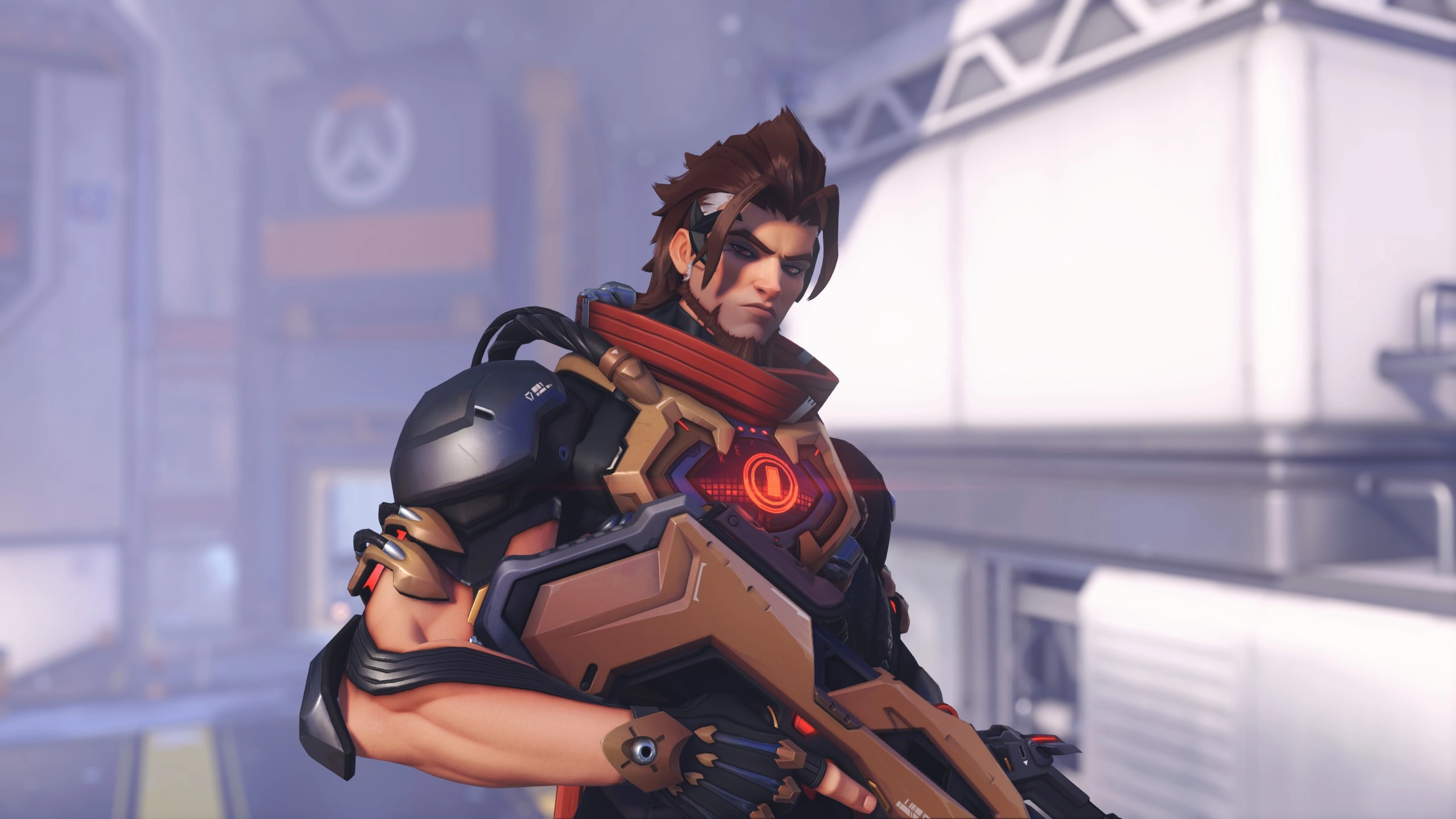 A new Overwatch hero in futuristic armor stands ready, holding a weapon, set in a high-tech environment