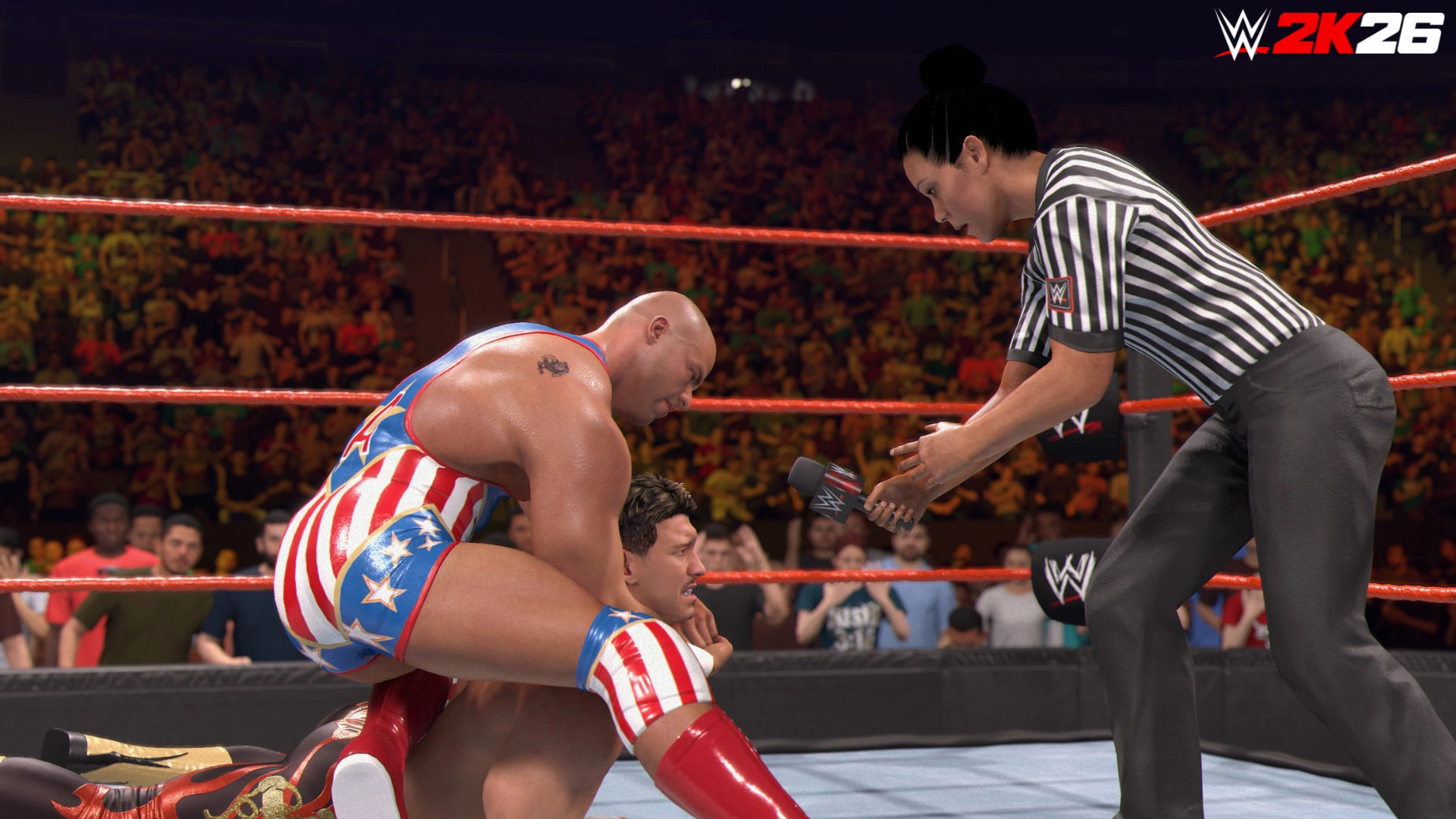 Wrestler in American flag attire holds opponent in a submission move as referee offers microphone