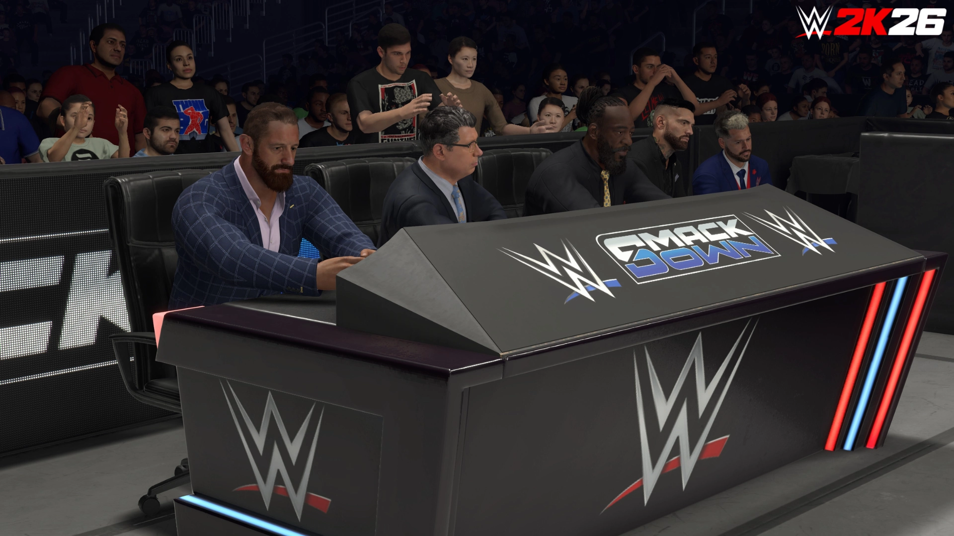 Commentary team at the SmackDown desk in WWE 2K26, with audience in the background during a match
